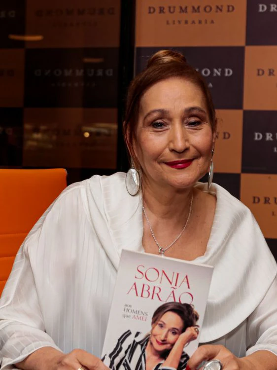 Sonia Abrão sorri em uma sessão de autógrafos na livraria, segurando seu livro Aos Homens que Amei.