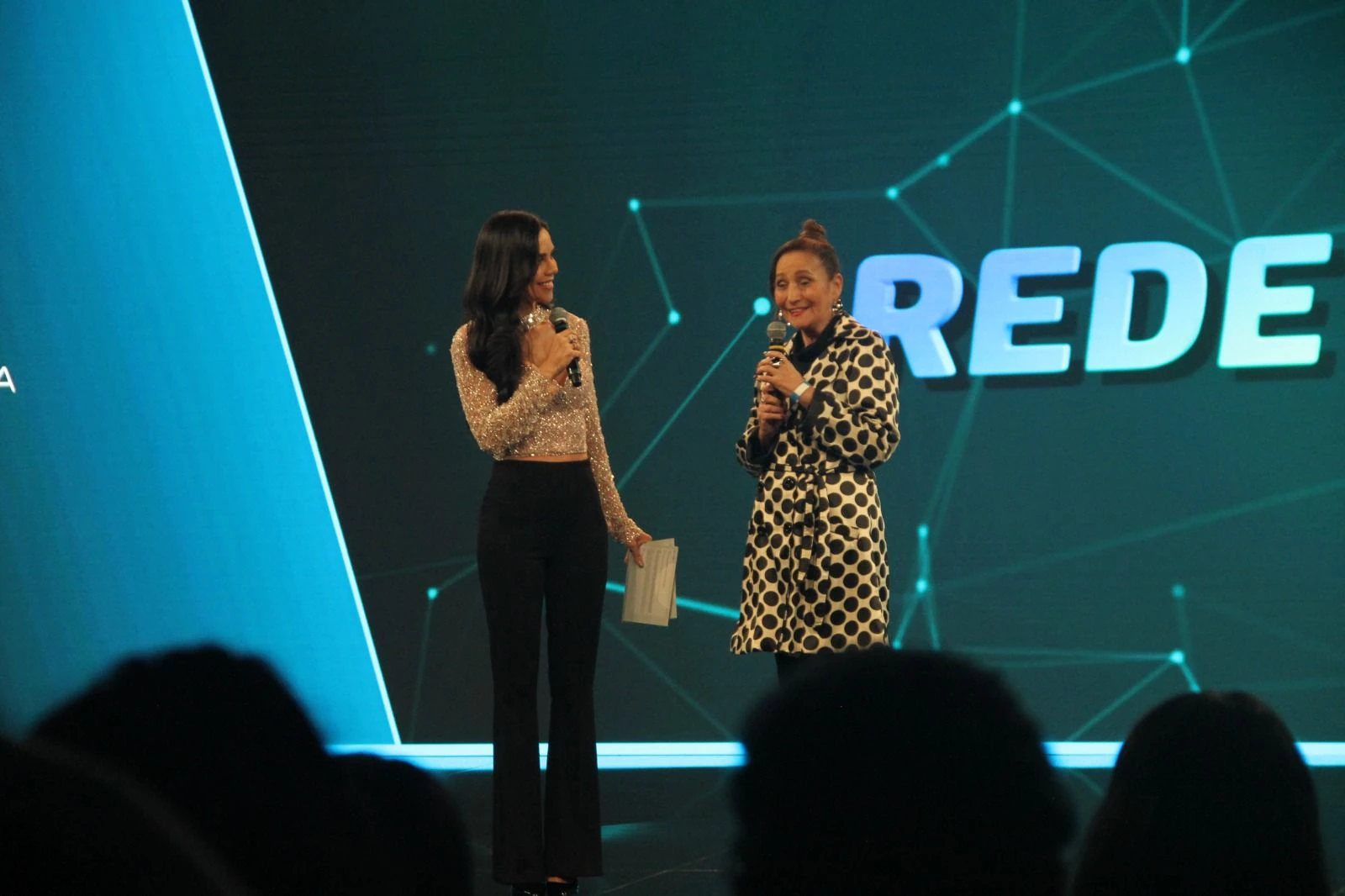 Sonia Abrão no palco da RedeTV!, de microfone na mão, em homenagem pelos 20 anos do A Tarde é Sua.